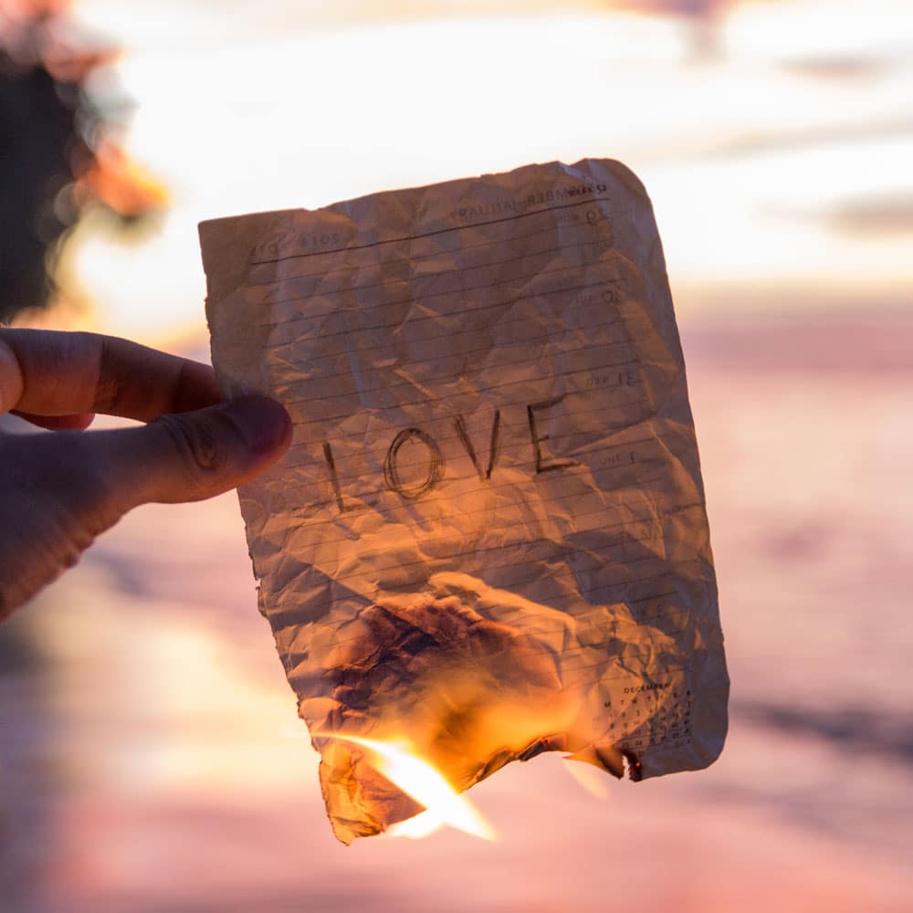 man burning paper that says "love"