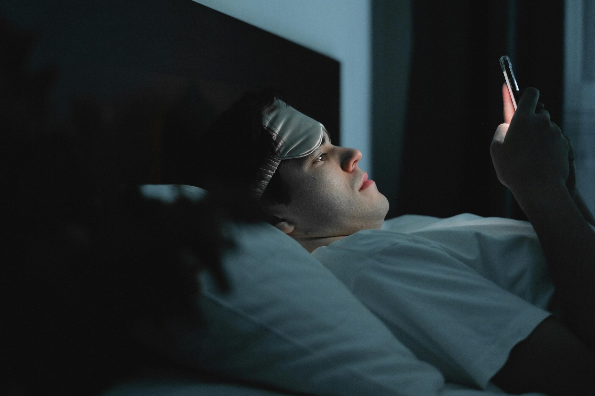 A young man addicted to porn looking at his cellphone in his bed in the dark